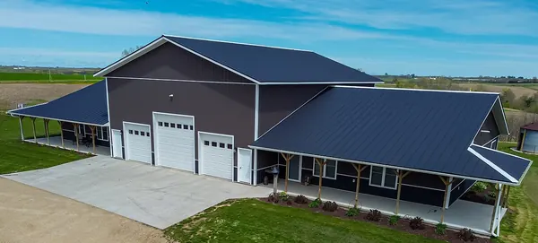 A dark metal barndominium with garage doors opening onto a concrete apron