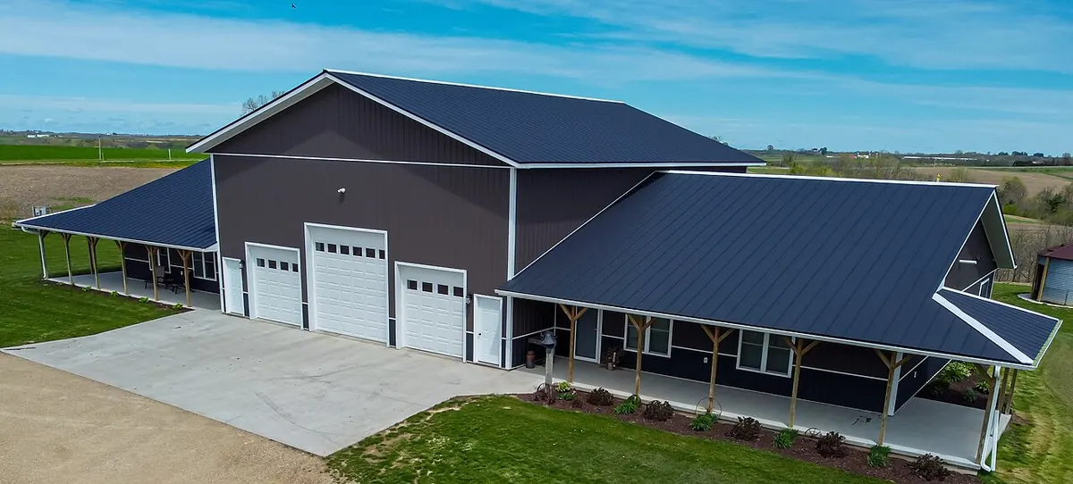 Dark metal barndominium with garage doors opening onto a concrete apron