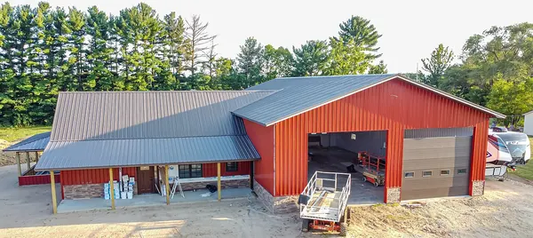 A red metal barndominium with an open shop bay on a gravel lot
