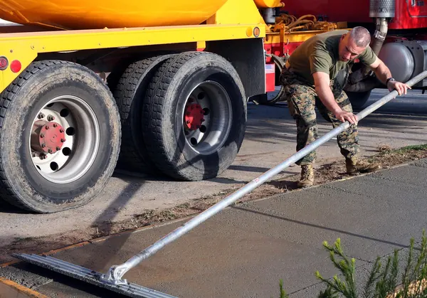 Marine smoothing a fresh concrete slab with a bull float beside a mixer truck