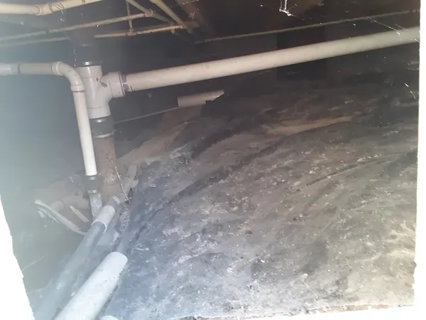 Crawl space under a house with plumbing pipes over bare soil
