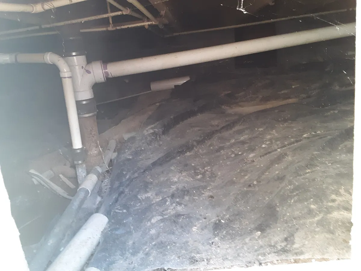 Crawl space under a house with plumbing pipes over bare soil