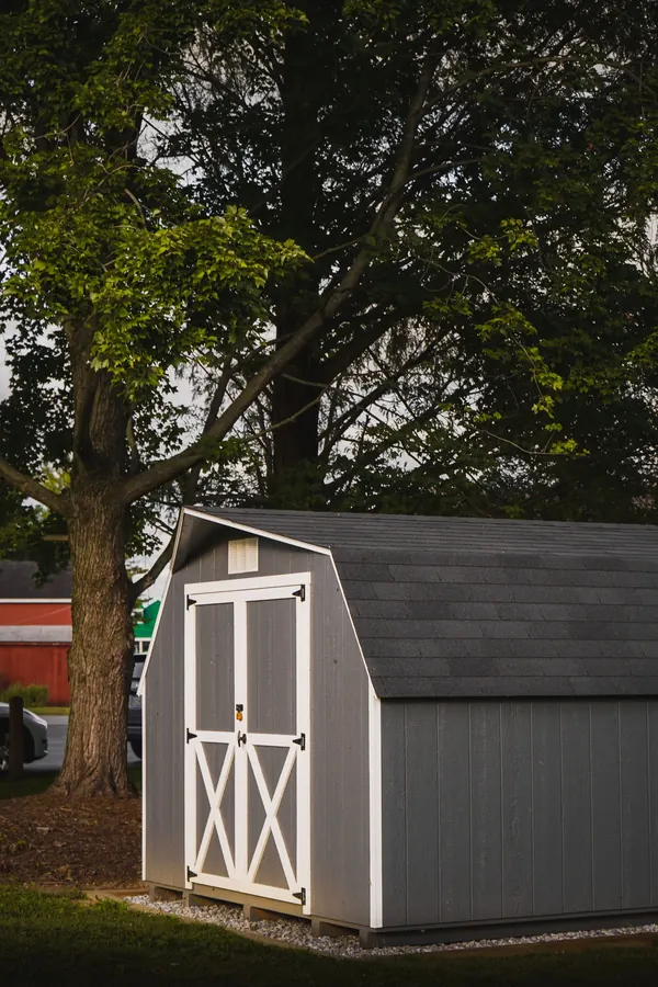 A gray storage shed sitting on the ground under trees in a backyard