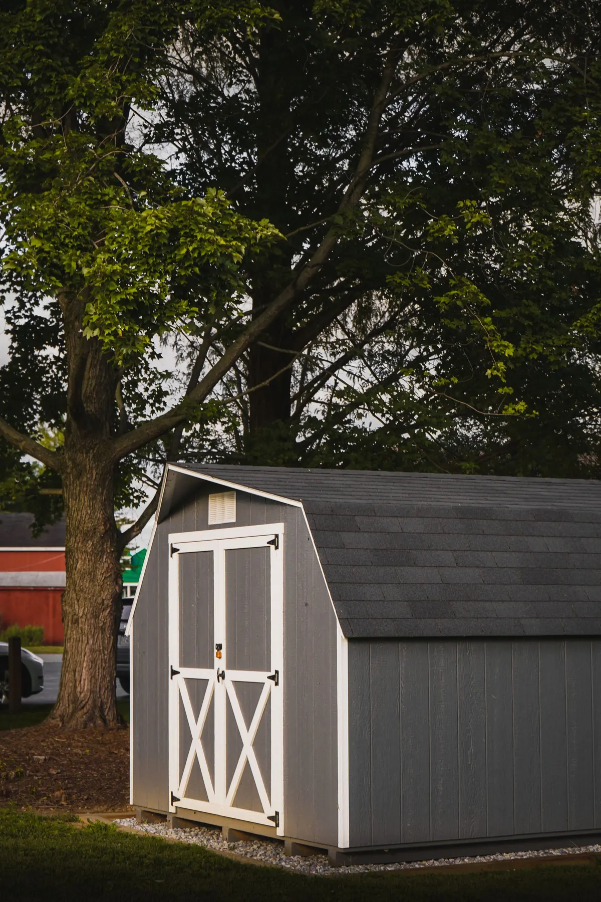 Gray storage shed sitting on the ground under trees in a backyard