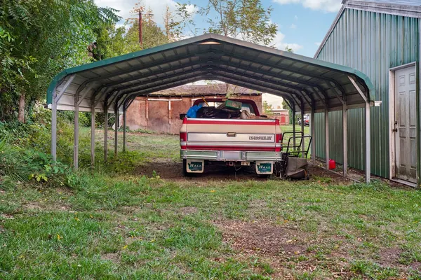 A pickup truck parked on grass under a metal carport
