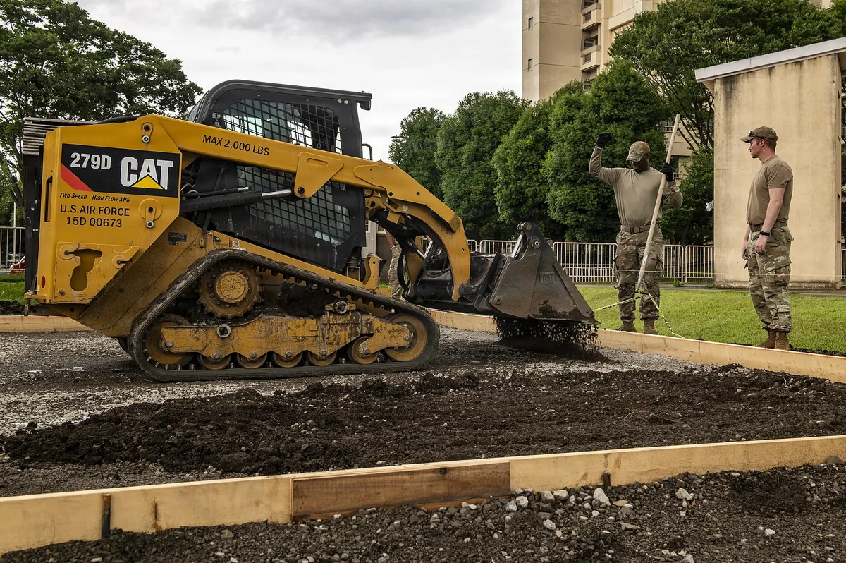 Wood forms set for a concrete pad while a skid steer spreads base