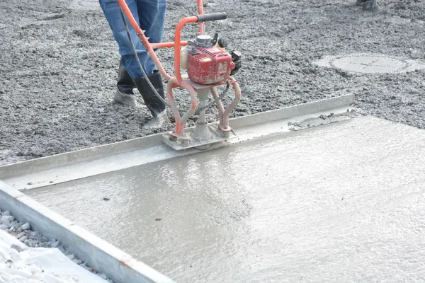 A worker running a vibrating power screed across a freshly poured slab