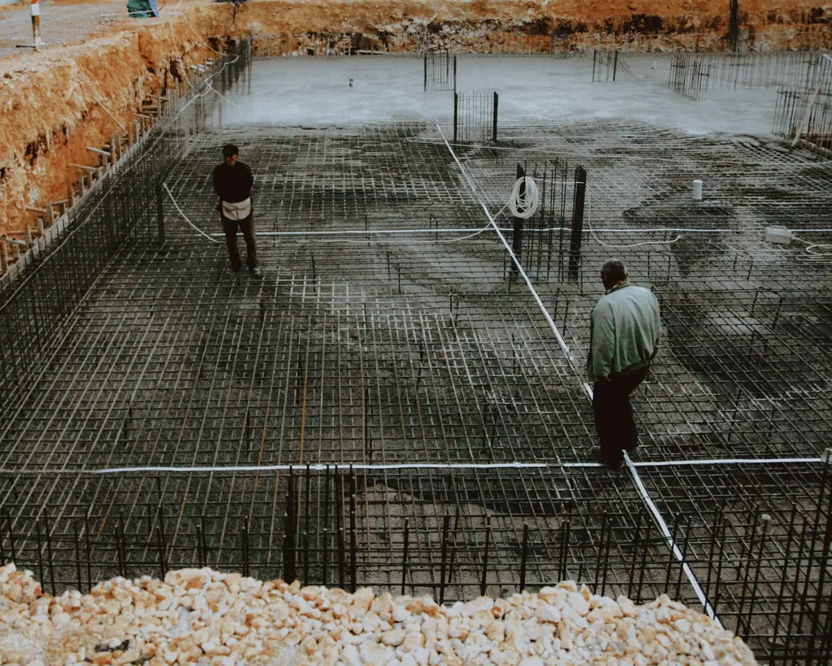 Workers on a tied rebar grid with a concrete pump hose before a large slab pour