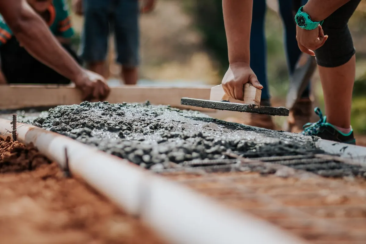 Hands striking off fresh concrete over wire mesh inside a form on red clay soil